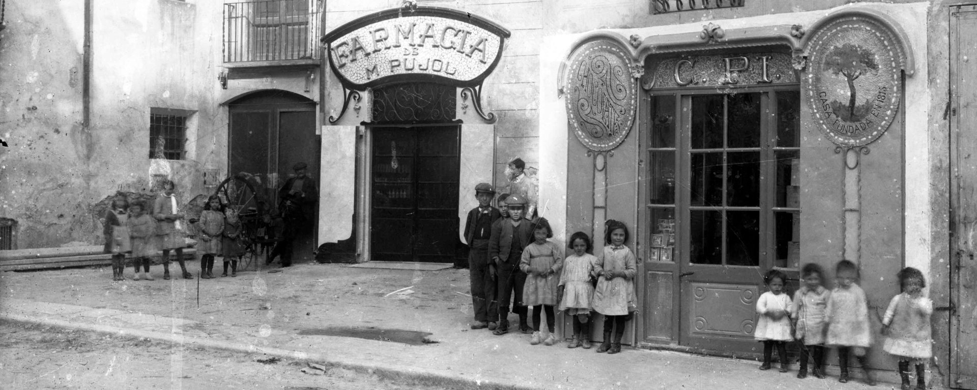 Retrat de grup davant la farmàcia de Martí Pujol i la xocolateria de Carles Pi, a Tortellà, 1918 (ACGAX. Fons Sadurní Brunet Pi. Foto: Sadurní Brunet. Codi atribuIt 28.1.4.2)
