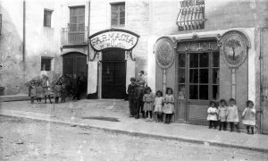 Retrat de grup davant la farmàcia de Martí Pujol i la xocolateria de Carles Pi, a Tortellà, 1918 (ACGAX. Fons Sadurní Brunet Pi. Foto: Sadurní Brunet. Codi atribuIt 28.1.4.2)